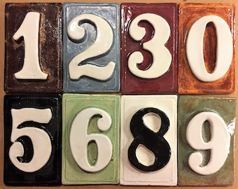 May include: Ten ceramic tiles with white numbers 1 through 9 and 0. Each tile has a different colored background. The tiles are arranged in two rows of five.