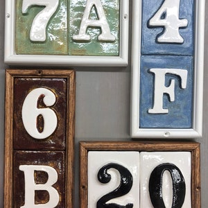 May include: A set of ceramic house numbers and letters in various colours and fonts. The numbers are 7A, 6B, 4F, and 20. The letters are in white and the numbers are in black.