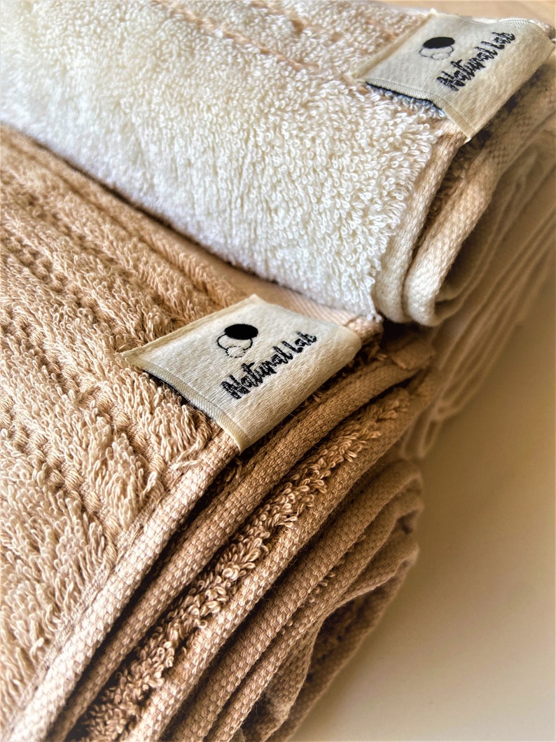 May include: Two rolled up towels, one beige and one white, with a Natural Lab label on each.