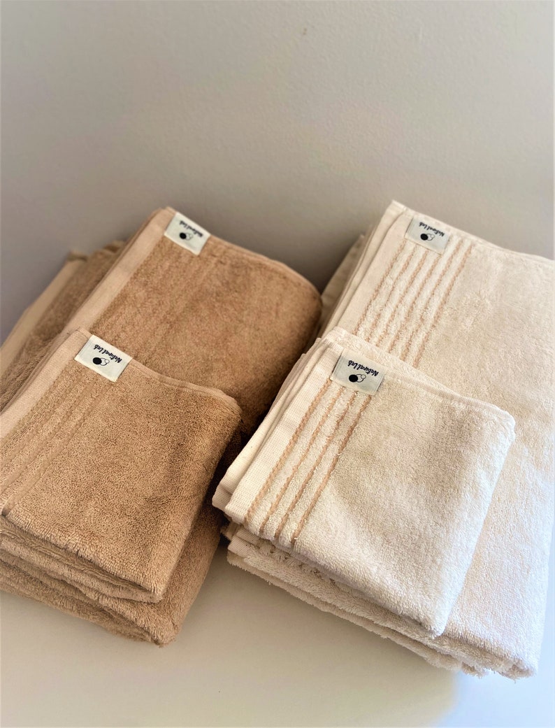 Peut inclure: Deux piles de serviettes, une en beige et une en blanc. Les serviettes beiges sont pli&eacute;es et empil&eacute;es, tandis que les serviettes blanches sont pli&eacute;es et empil&eacute;es avec quelques serviettes sur le dessus. Les serviettes portent une &eacute;tiquette noire avec le mot "remarquable" dessus.