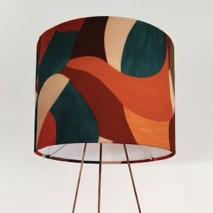 Peut inclure: Un lampadaire moderne avec une structure en métal cuivré. L'abat-jour présente un motif abstrait dans des tons orange, vert d'eau, marron et beige. Le design de la lampe est minimaliste et élégant, adapté aux intérieurs contemporains.
