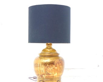 May include: A gold ceramic table lamp with a black fabric lampshade. The lamp base is shaped like a jar with a lid.