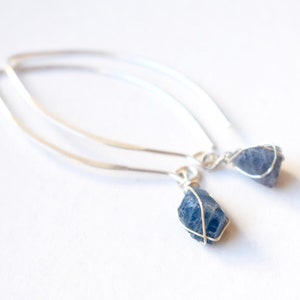 May include: A pair of silver earrings with blue gemstone drops. The gemstones are wrapped in silver wire.