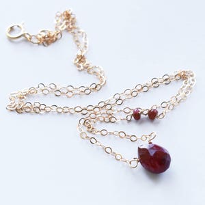 May include: A gold chain necklace with a teardrop-shaped red gemstone pendant and two smaller red gemstones on the chain.