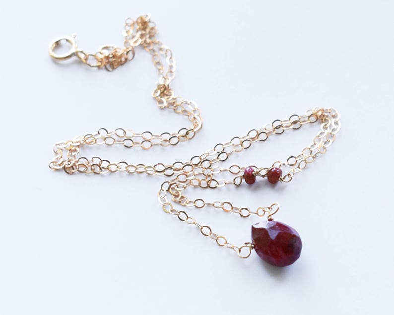 May include: A gold chain necklace with a teardrop-shaped red gemstone pendant and two smaller red gemstones on the chain.