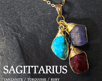 May include: Gold chain necklace with a pendant featuring three wrapped gemstones: turquoise, tanzanite, and ruby. The pendant is labeled "SAGITTARIUS" with the text "TANZANITE / TURQUOISE / RUBY CITRINE / AMETHYST / AQUAMARINE".