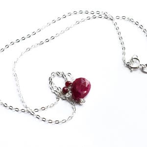 May include: A silver chain necklace with a red gemstone pendant. The pendant is a faceted ruby with smaller ruby accents.