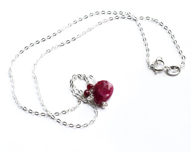 May include: A silver chain necklace with a red gemstone pendant. The pendant is a faceted ruby with smaller ruby accents.