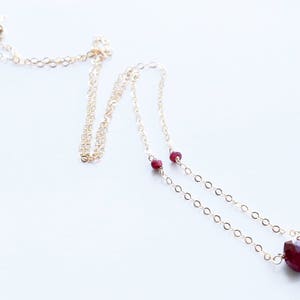 May include: A delicate gold chain necklace with a ruby pendant and two smaller ruby accents. The necklace is on a white background.