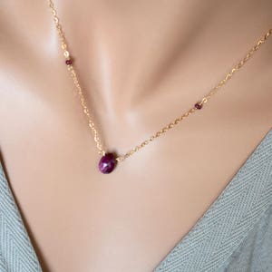 May include: A gold chain necklace with a single ruby gemstone pendant and two smaller ruby accents.