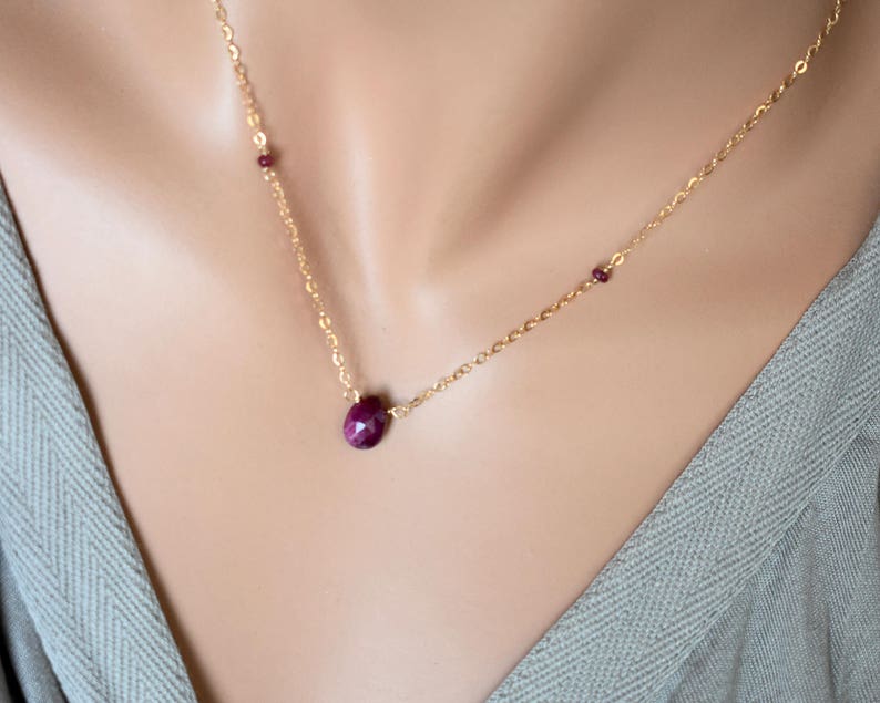 May include: A gold chain necklace with a single ruby gemstone pendant and two smaller ruby accents.