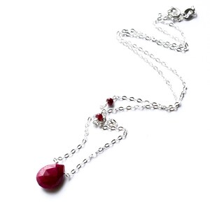 May include: A silver chain necklace with a teardrop-shaped ruby pendant and smaller ruby accents.