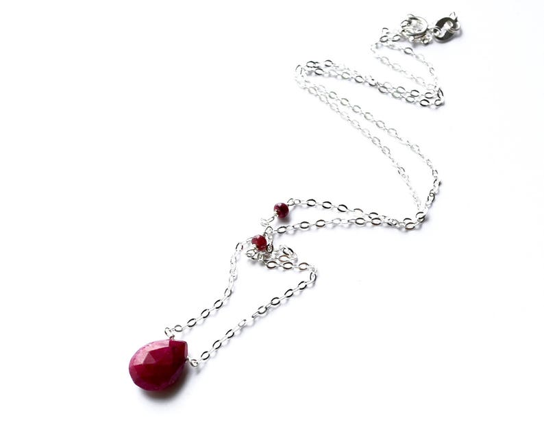 May include: A silver chain necklace with a teardrop-shaped ruby pendant and smaller ruby accents.