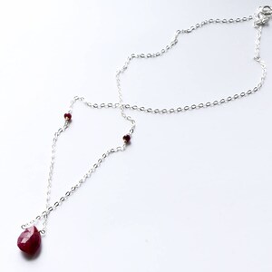 May include: A silver chain necklace with a teardrop-shaped ruby pendant and small ruby accents.
