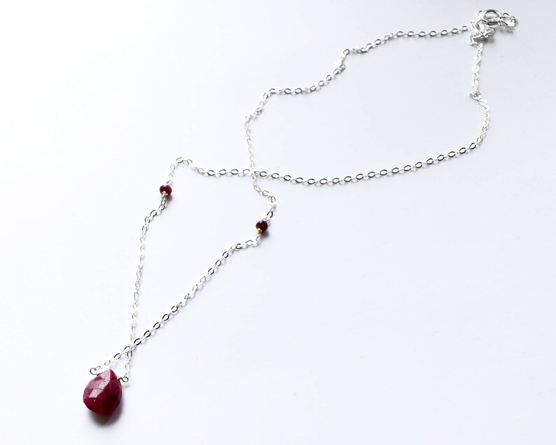 May include: A silver chain necklace with a teardrop-shaped ruby pendant and small ruby accents.