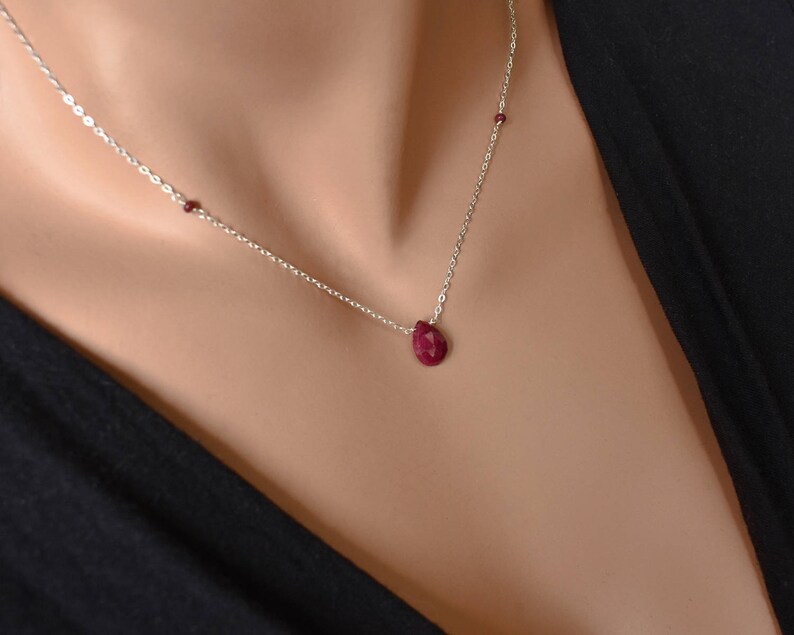 May include: A silver chain necklace with a teardrop-shaped ruby pendant and two smaller ruby accents.