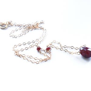 May include: A gold chain necklace with a large, faceted, red gemstone pendant and two smaller red gemstone accents.