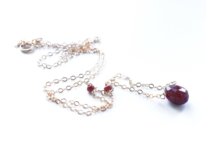 May include: A gold chain necklace with a large, faceted, red gemstone pendant and two smaller red gemstone accents.