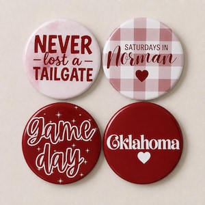 May include: Four circular pin-back buttons with red and white designs. One says NEVER lost a TAILGATE, one says SATURDAYS IN Norman with a heart, one says Game day with star accents, and one says Oklahoma with a heart. All feature red text and graphics.