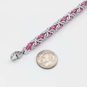 May include: A pink and silver chainmail bracelet with a lobster clasp. The bracelet is about the size of a dime.