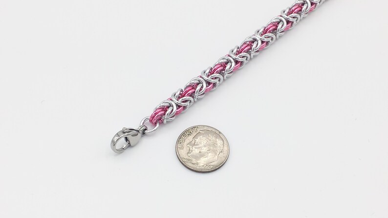 May include: A pink and silver chainmail bracelet with a lobster clasp. The bracelet is about the size of a dime.