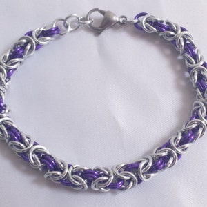 May include: A handmade bracelet featuring a chainmail design with alternating silver-tone and purple links. The bracelet has a lobster clasp closure and is displayed on a white surface. Jewelry.
