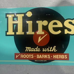K&ouml;nnte beinhalten: Vintage Hires-Schild mit t&uuml;rkisblauem Hintergrund und gelber Schrift. Das Wort "Hires" ist prominent &uuml;ber einem roten Kreis mit einem H&auml;kchen dargestellt. Das Schild besagt auch "made with roots, barks, herbs."