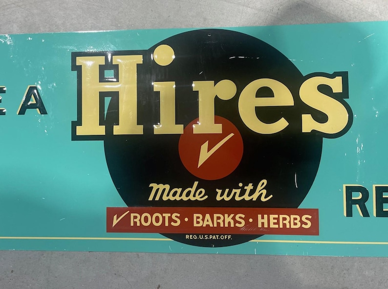 K&ouml;nnte beinhalten: Vintage Hires-Schild mit t&uuml;rkisblauem Hintergrund und gelber Schrift. Das Wort "Hires" ist prominent &uuml;ber einem roten Kreis mit einem H&auml;kchen dargestellt. Das Schild besagt auch "made with roots, barks, herbs."