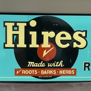K&ouml;nnte beinhalten: Ein rechteckiges Schild im Vintage-Stil mit t&uuml;rkisfarbenem Hintergrund. Auf dem Schild steht "HAVE A Hires AND REFRESH" in fetter, gelber und schwarzer Schrift. In der Mitte befindet sich ein schwarzer Kreis mit einem roten H&auml;kchen und den Worten "Made with ROOTS &bull; BARKS &bull; HERBS".