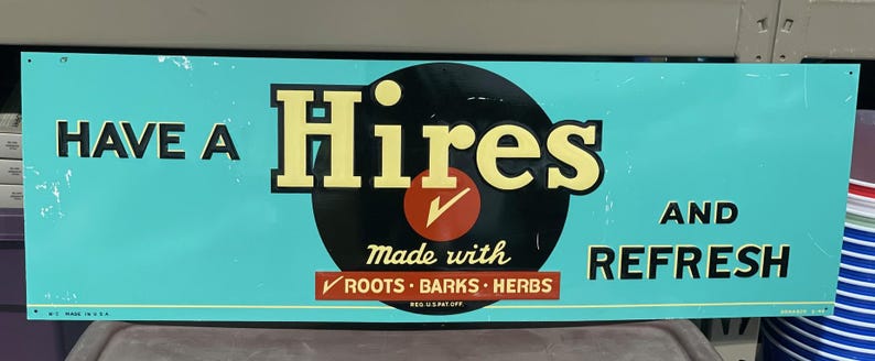 K&ouml;nnte beinhalten: Ein rechteckiges Schild im Vintage-Stil mit t&uuml;rkisfarbenem Hintergrund. Auf dem Schild steht "HAVE A Hires AND REFRESH" in fetter, gelber und schwarzer Schrift. In der Mitte befindet sich ein schwarzer Kreis mit einem roten H&auml;kchen und den Worten "Made with ROOTS &bull; BARKS &bull; HERBS".