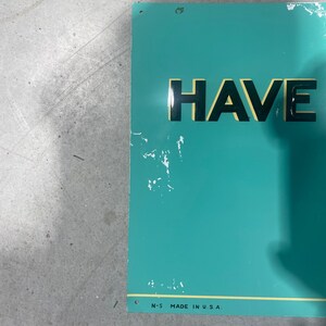 K&ouml;nnte beinhalten: Ein rechteckiges, t&uuml;rkisfarbenes Metallschild mit dem Wort "HAVE" in fetten schwarzen Buchstaben. Das Schild hat einen gelben Rand und den Text "N-5 MADE IN U.S.A." unten. Es gibt einige wei&szlig;e Farbsplitter auf dem Schild.