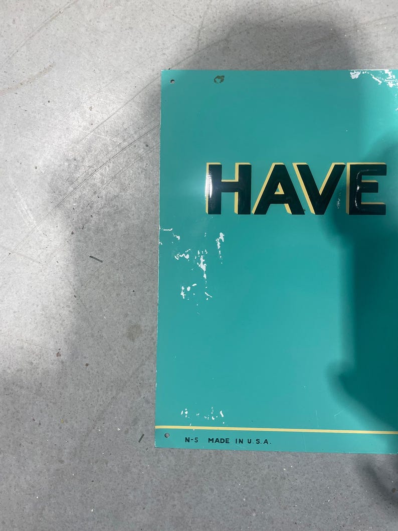 K&ouml;nnte beinhalten: Ein rechteckiges, t&uuml;rkisfarbenes Metallschild mit dem Wort "HAVE" in fetten schwarzen Buchstaben. Das Schild hat einen gelben Rand und den Text "N-5 MADE IN U.S.A." unten. Es gibt einige wei&szlig;e Farbsplitter auf dem Schild.
