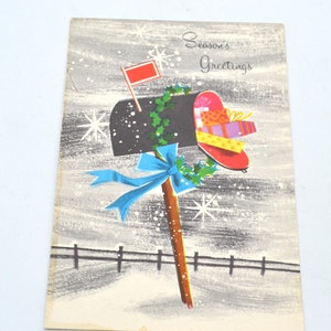 May include: A vintage Christmas card featuring a black mailbox with a red flag, decorated with holly and overflowing with colorful gifts. The mailbox is on a wooden post with a blue ribbon and is set against a snowy background with the text "Season's Greetings".