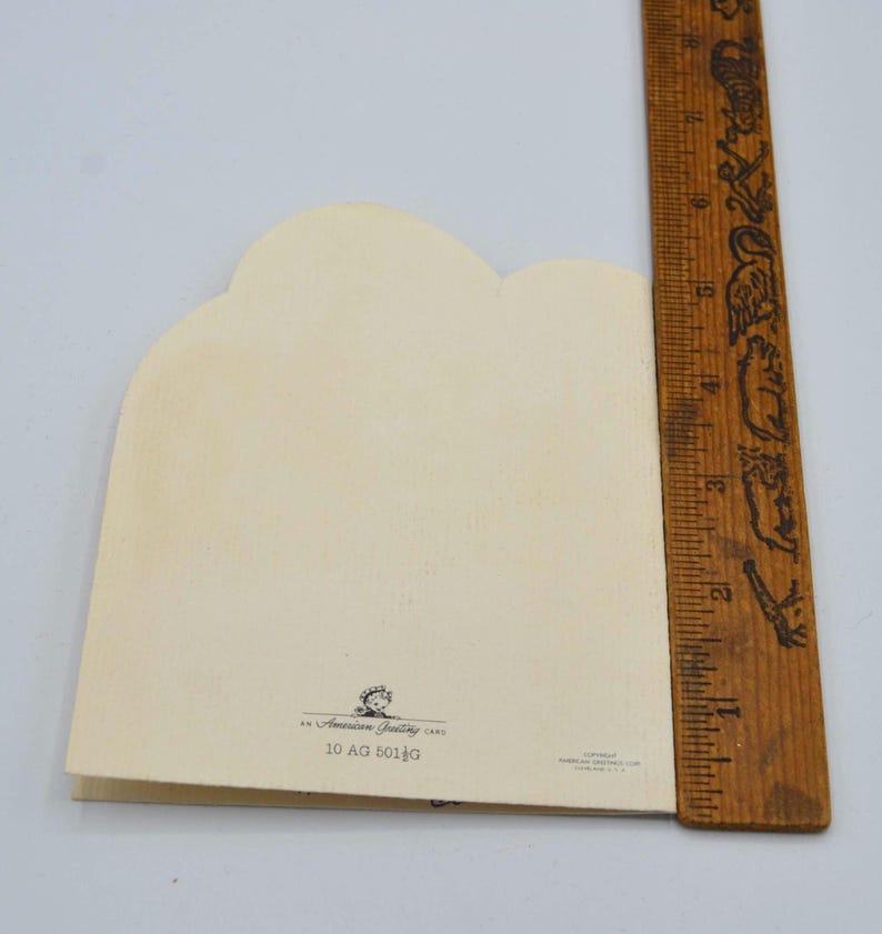 Puede incluir: Una tarjeta de felicitaci&oacute;n vintage con un borde superior festoneado, papel color crema y una regla de madera. La tarjeta tiene el texto "An American Greeting Card" y "10 AG 501G" impreso. La regla est&aacute; marcada en pulgadas, aproximadamente 15 cm.