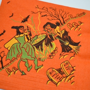 May include: Orange Halloween-themed paper napkin with a green devil, two witches, and a cauldron with flames. The witches are stirring the cauldron with broomsticks. There are tombstones with "RIP" written on them.