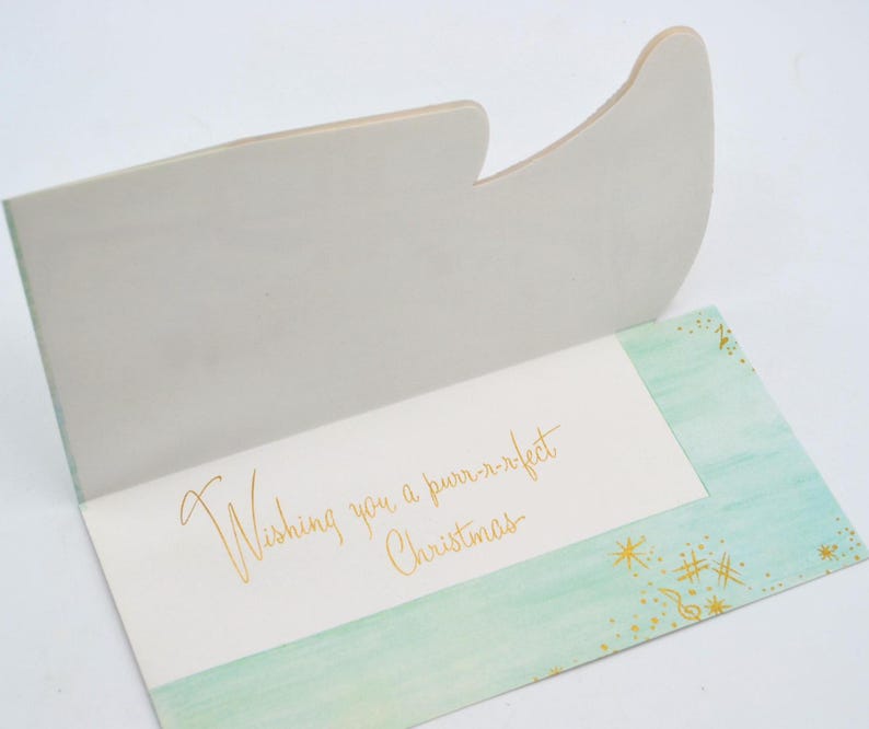 May include: A light green card with a gold glitter design and the text "Wishing you a purr-r-fect Christmas".