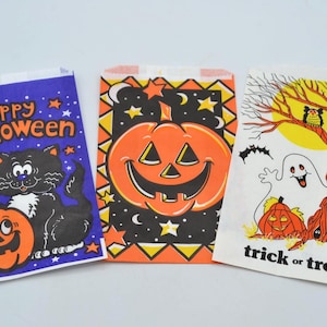 May include: Three vintage Halloween treat bags. One bag features a black cat and pumpkin with the words "Happy Halloween." Another has a jack-o'-lantern design. The third bag has a ghost, owl, and tree with the words "trick or treat."