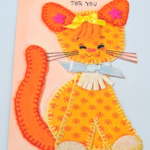 May include: A vintage greeting card featuring a felt appliqué of an orange cat with a yellow bow and pink flowers. The card has the text "FOR YOU" printed on it.