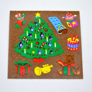 May include: A sheet of brown paper with colorful Christmas stickers. The stickers include a Christmas tree, a stocking, a present, a toy drum, a teddy bear holding a present, a trumpet, and a toy with a star on top.