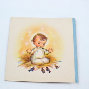 May include: A vintage Christmas card featuring a baby Jesus in a manger with a halo of stars and birds surrounding him. The card is cream colored with a blue border.