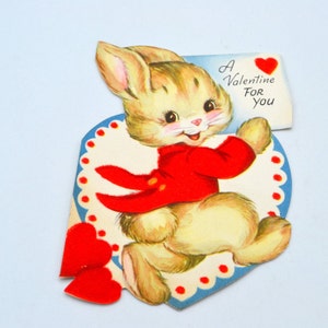 May include: A vintage Valentine's Day card featuring a cartoon bunny wearing a red coat and holding a heart-shaped envelope that says "A Valentine For You".