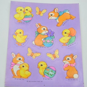 May include: A sheet of vintage Easter stickers featuring bunnies and chicks. The stickers are on a purple background and feature a variety of designs, including bunnies holding eggs, chicks with eggs, and butterflies. The stickers are from 1984 Hallmark Cards, Inc.