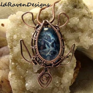 May include: A copper wire wrapped pendant featuring a blue and white agate cabochon. The pendant is shaped like a turtle and has a detailed design.