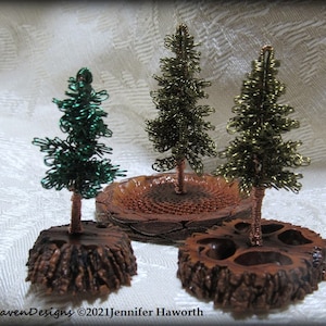 Pode incluir: Três árvores de Natal em miniatura envoltas em arame em bases de madeira. As árvores são verdes, douradas e azul-esverdeadas. As árvores estão sobre um fundo branco.