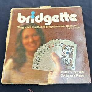 May include: A vintage board game box for Bridgette, a two-handed bridge game. The box features a woman holding a hand of cards, with the text "The greatest two-handed bridge game ever conceived." and "OSWALD JACOBY".