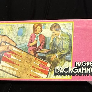 May include: A vintage pink box with the words "MAGNETIC BACKGAMMON" in white. The box features a retro illustration of a backgammon game in progress on an airplane. The game board is visible, along with two people playing.
