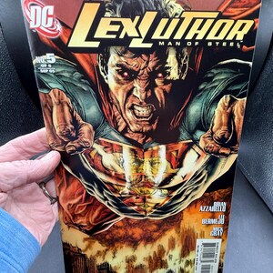 May include: A comic book cover for "Lex Luthor: Man of Steel" No. 5, featuring a close-up of a menacing Superman-like figure with red eyes. The cover has a red and blue color scheme with the DC Comics logo and the issue number.