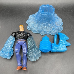 May include: A superhero action figure with blue water-like arms, black top, and blue pants. Includes a blue water-themed base and accessories. The figure has blonde hair and brown boots. The accessories include a water spout and a water-like structure.