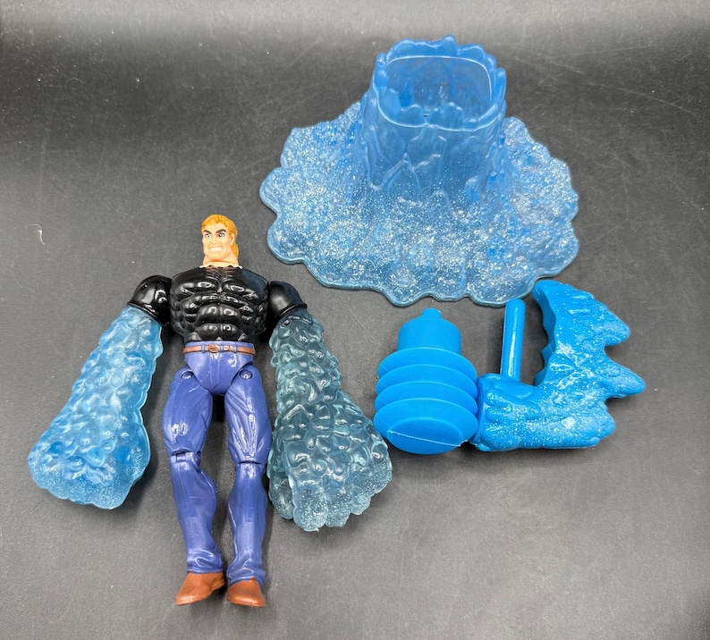 May include: A superhero action figure with blue water-like arms, black top, and blue pants. Includes a blue water-themed base and accessories. The figure has blonde hair and brown boots. The accessories include a water spout and a water-like structure.