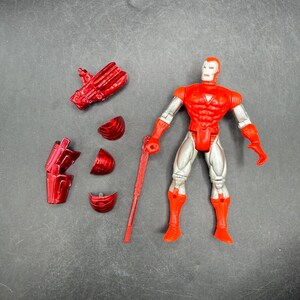 Puede incluir: Una figura de acci&oacute;n roja y plateada de un superh&eacute;roe con piezas de armadura desmontables y un bast&oacute;n rojo. La figura tiene un torso, brazos y piernas rojos, con detalles plateados. La figura est&aacute; de pie.